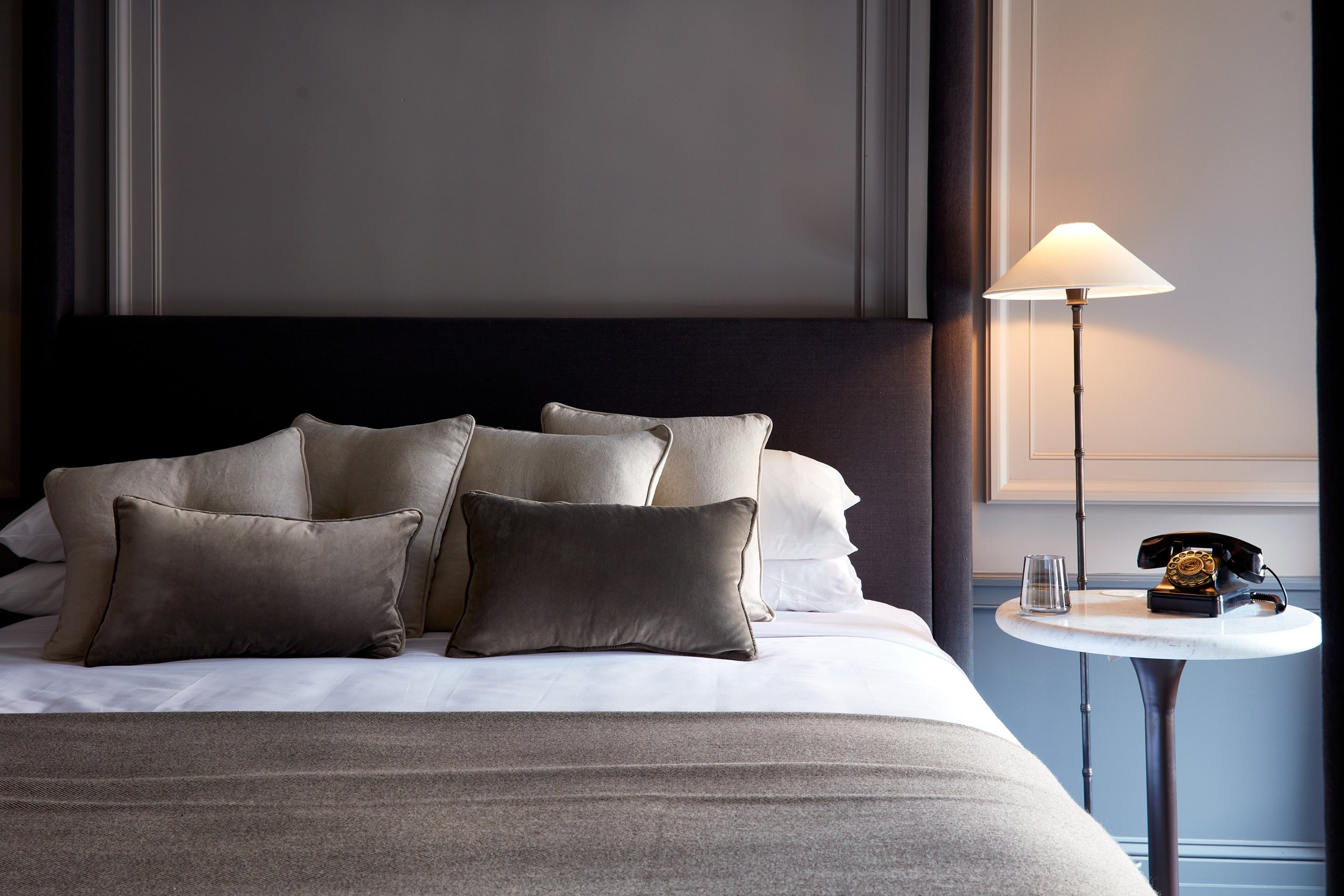 A close up photo of a king bed with a night stand and a turned-on lamp to the right.