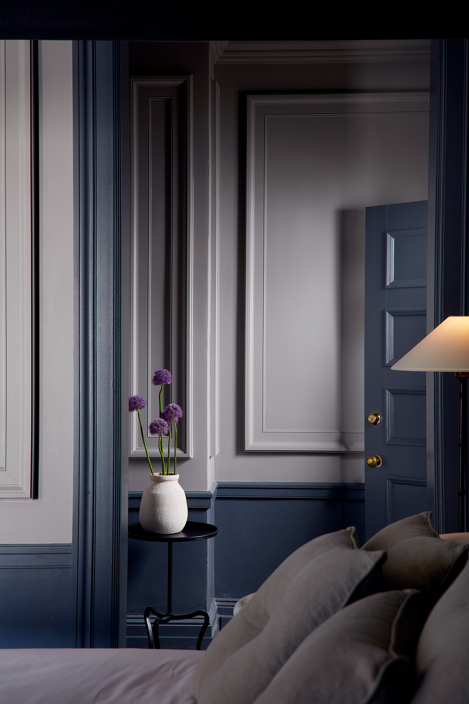 A closeup of a bed from the side into a wall with deep bluish gray walls and ornate molding.