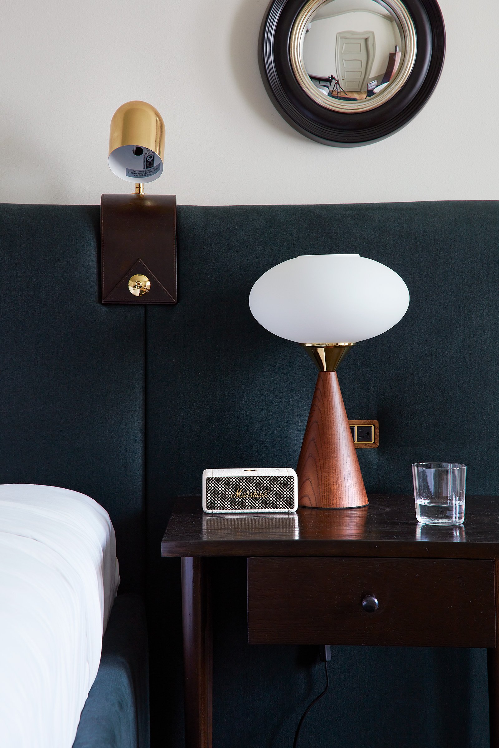 A closeup of a bedside lamp with an upholstered headboard