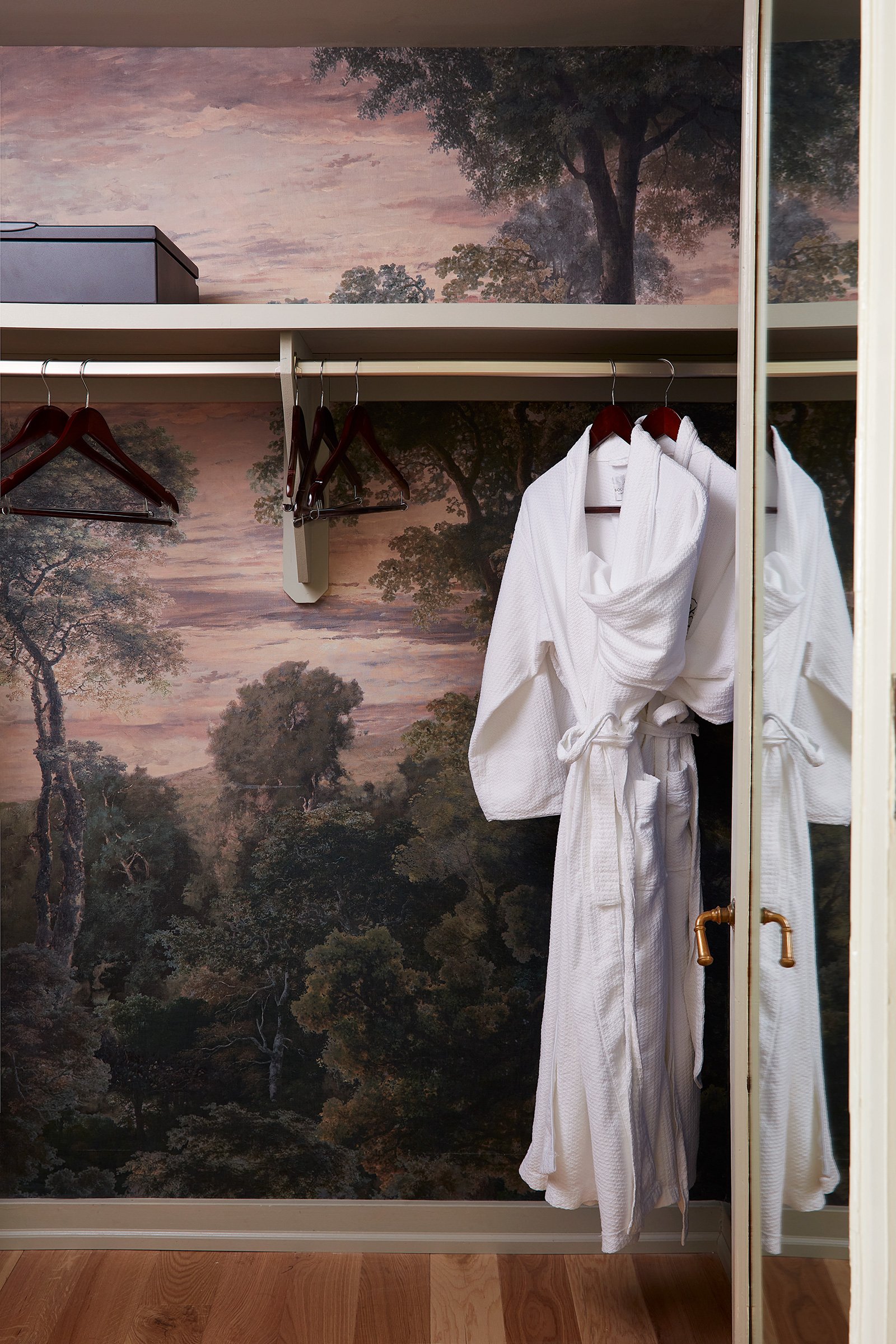 A muraled wallpapered closet with two plush white robes hanging.