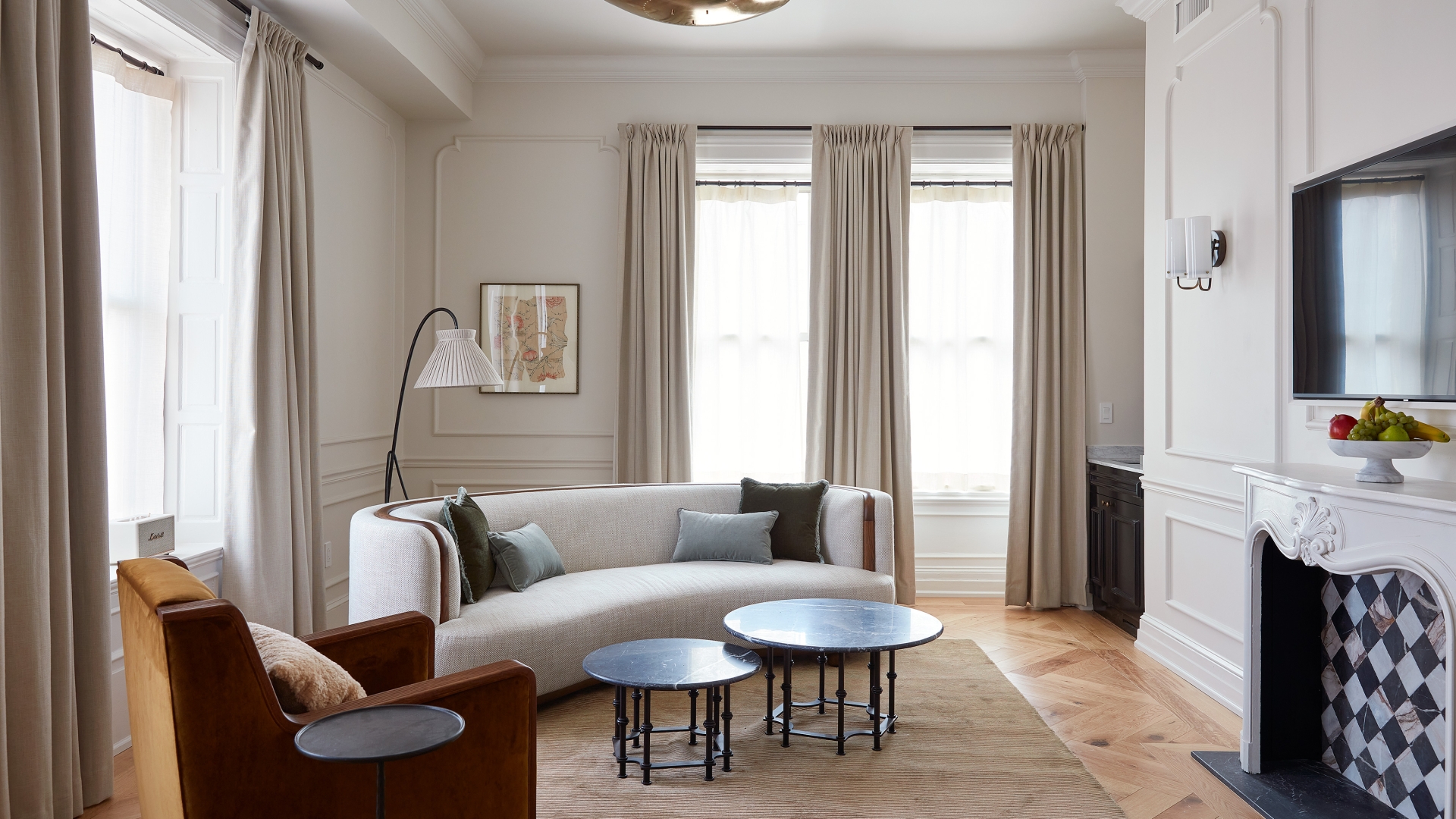 A white walled living room with wall moldings and a fireplace. There is a curved sofa and armchair with a reading lamp behind.