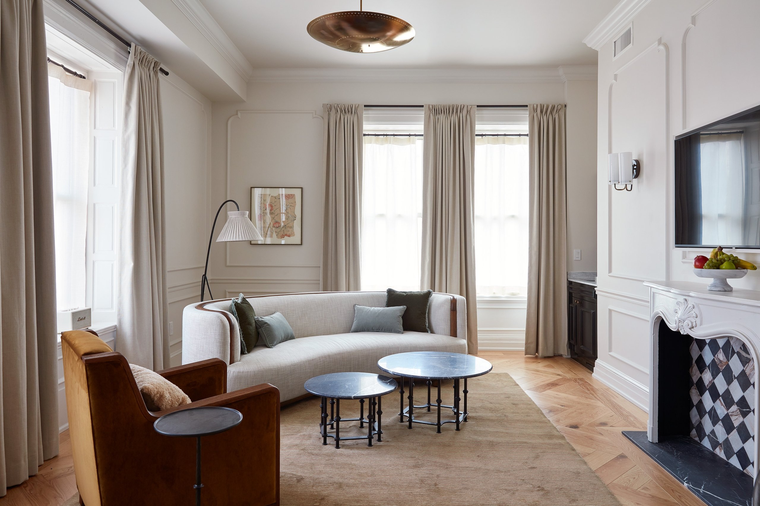 A white walled living room with wall moldings and a fireplace. There is a curved sofa and armchair with a reading lamp behind.