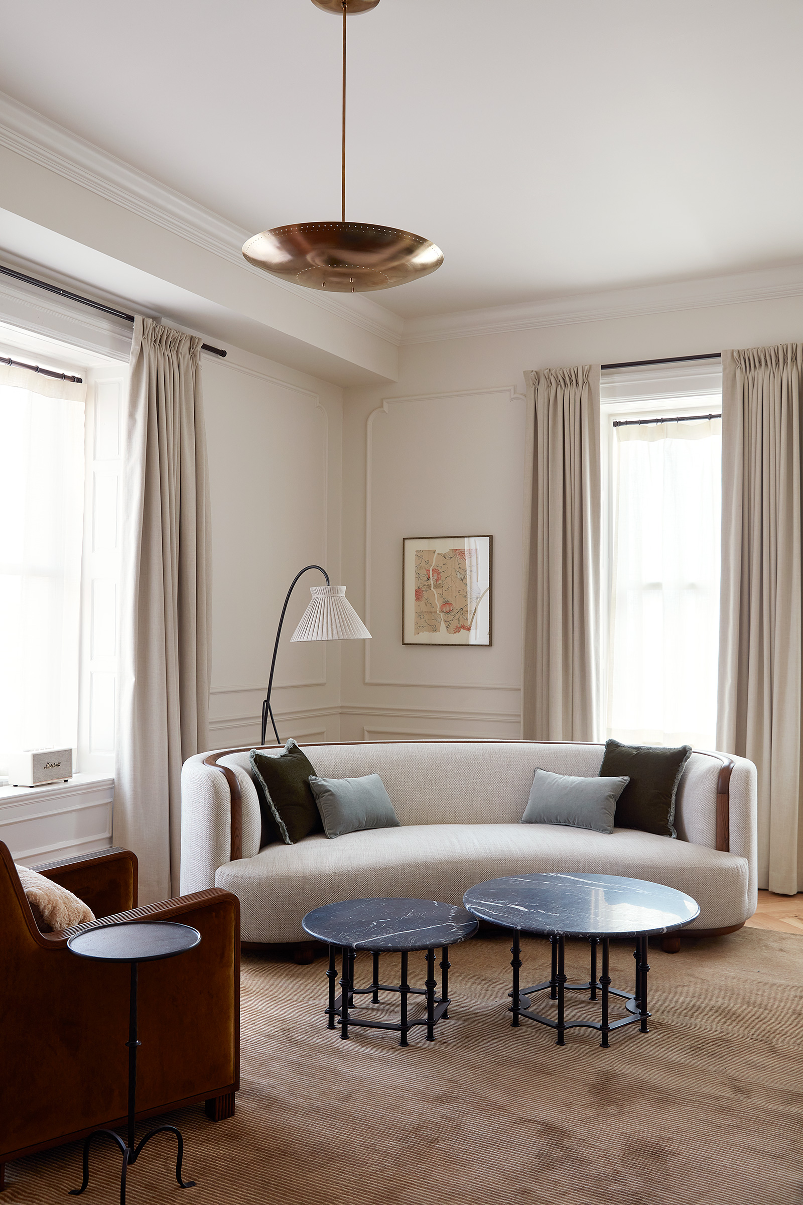 A white walled living room with wall moldings and a fireplace. There is a curved sofa and armchair with a reading lamp behind.