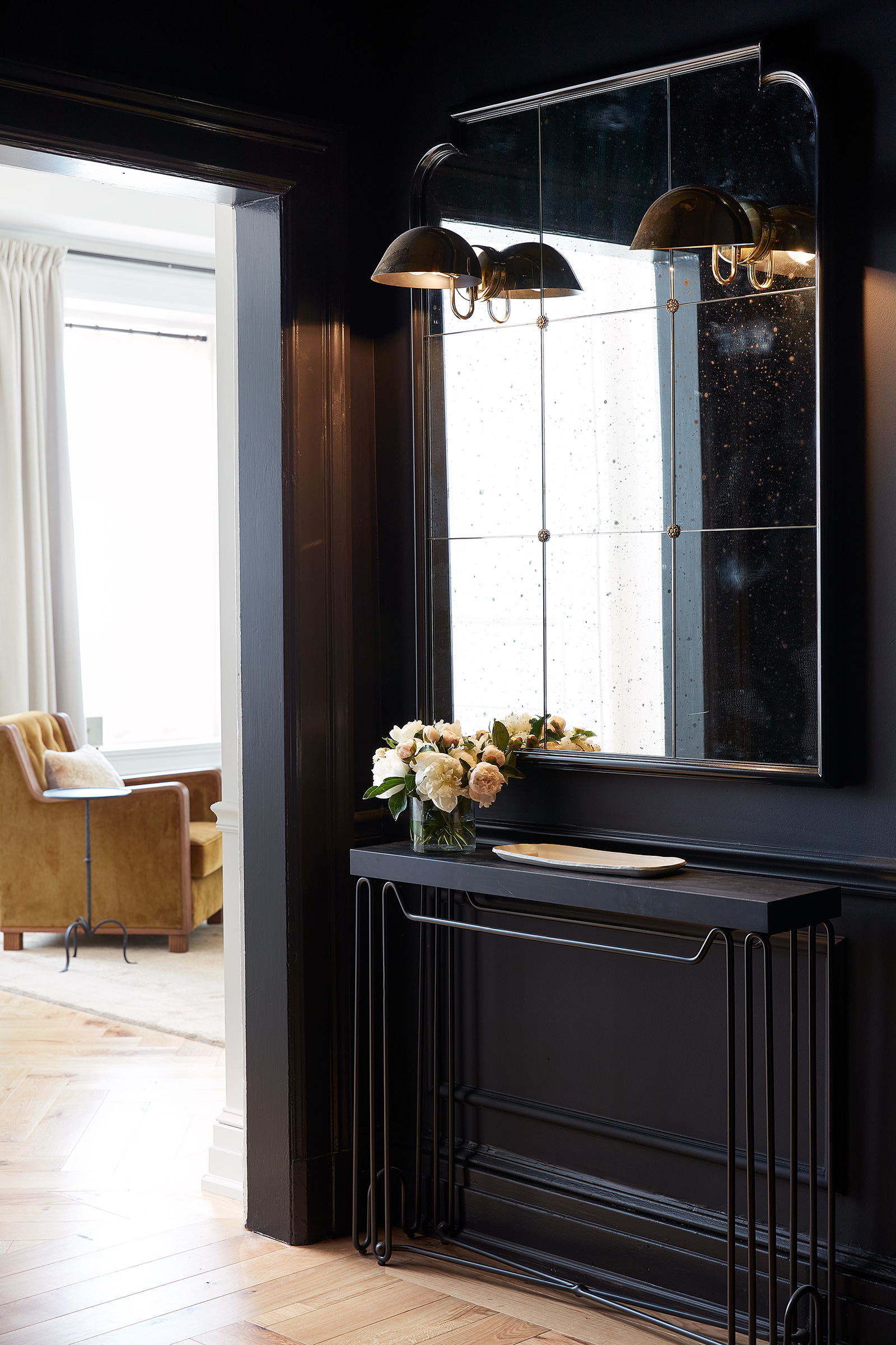 A black walled foyer with antiqued mirror looking into a living room