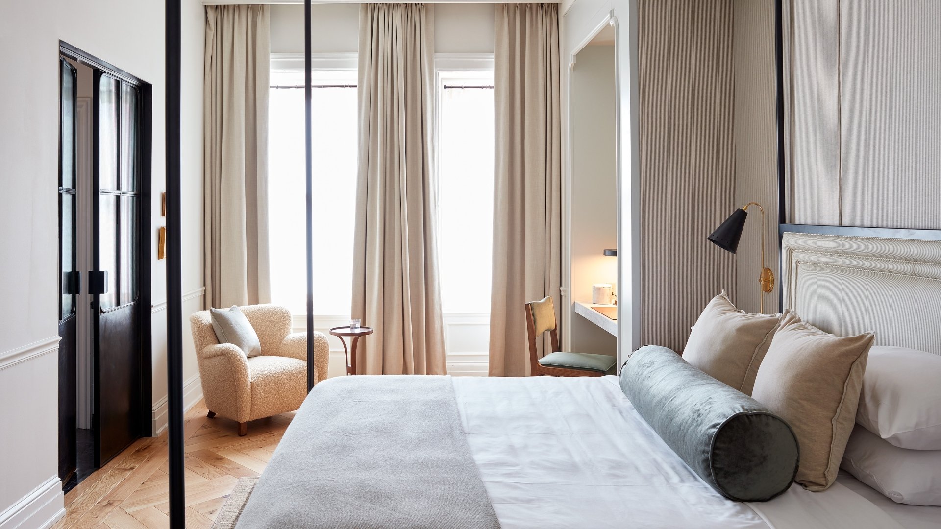 A canopy bed and small sitting area facing two tall windows