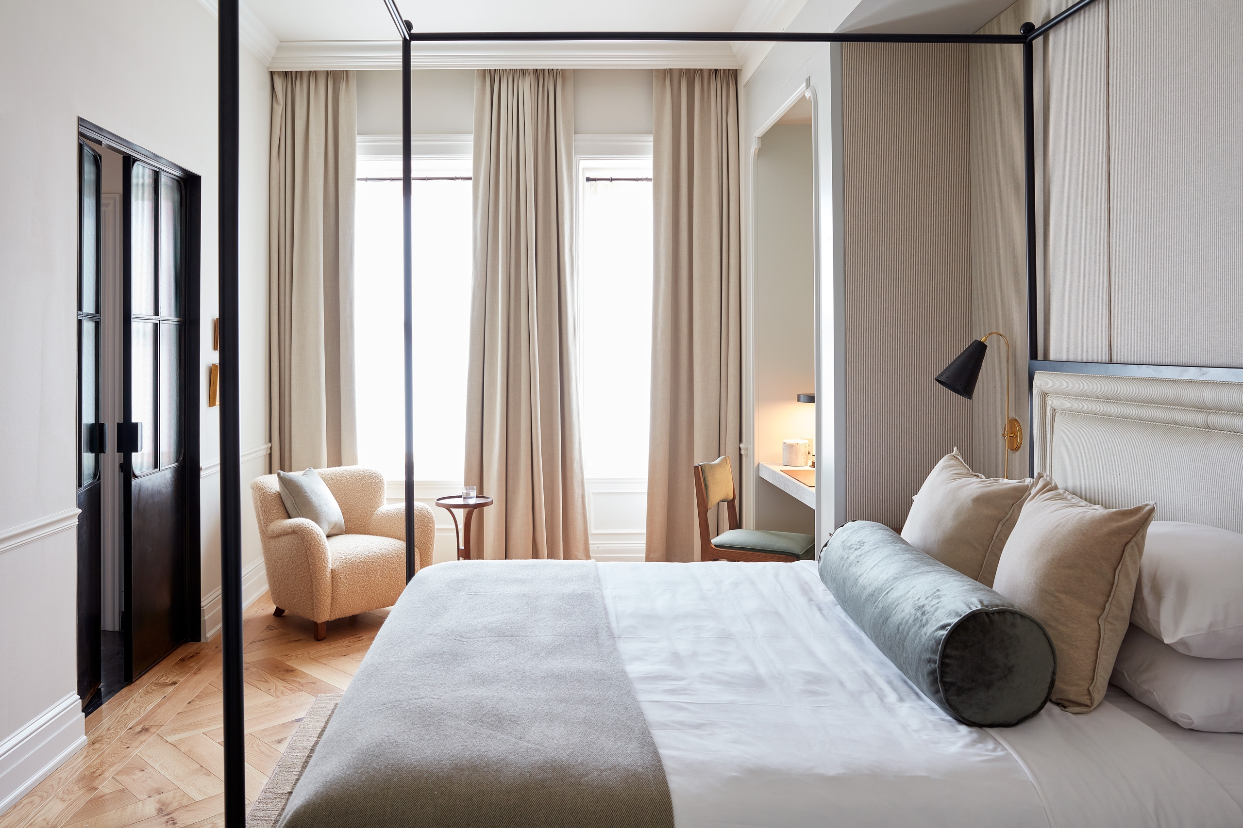 A canopy bed and small sitting area facing two tall windows