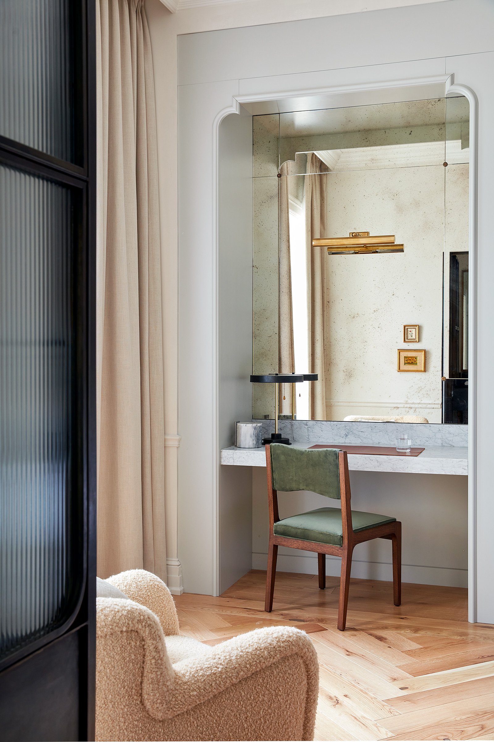 A desk area with combination vanity-work-table facing a coved mirror with an upholstered chair