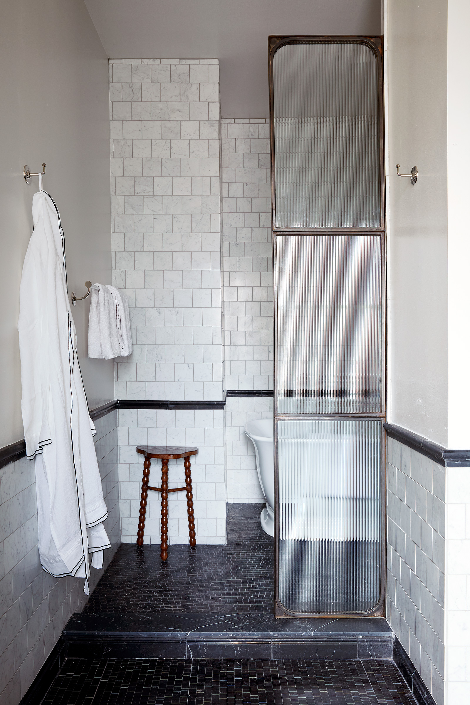 A black marble tile bathroom with white marble tile walls. There is a paneled glass divider in front of a free-standing bathtub.