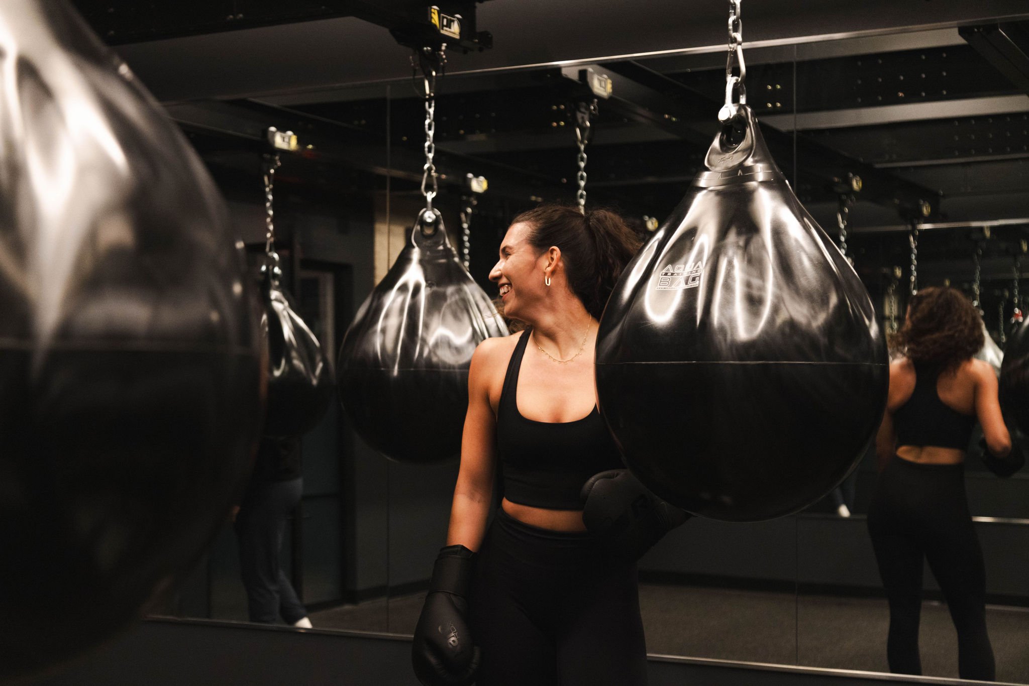 A woman facing away from camera with boxing gloves, facing a punching bag