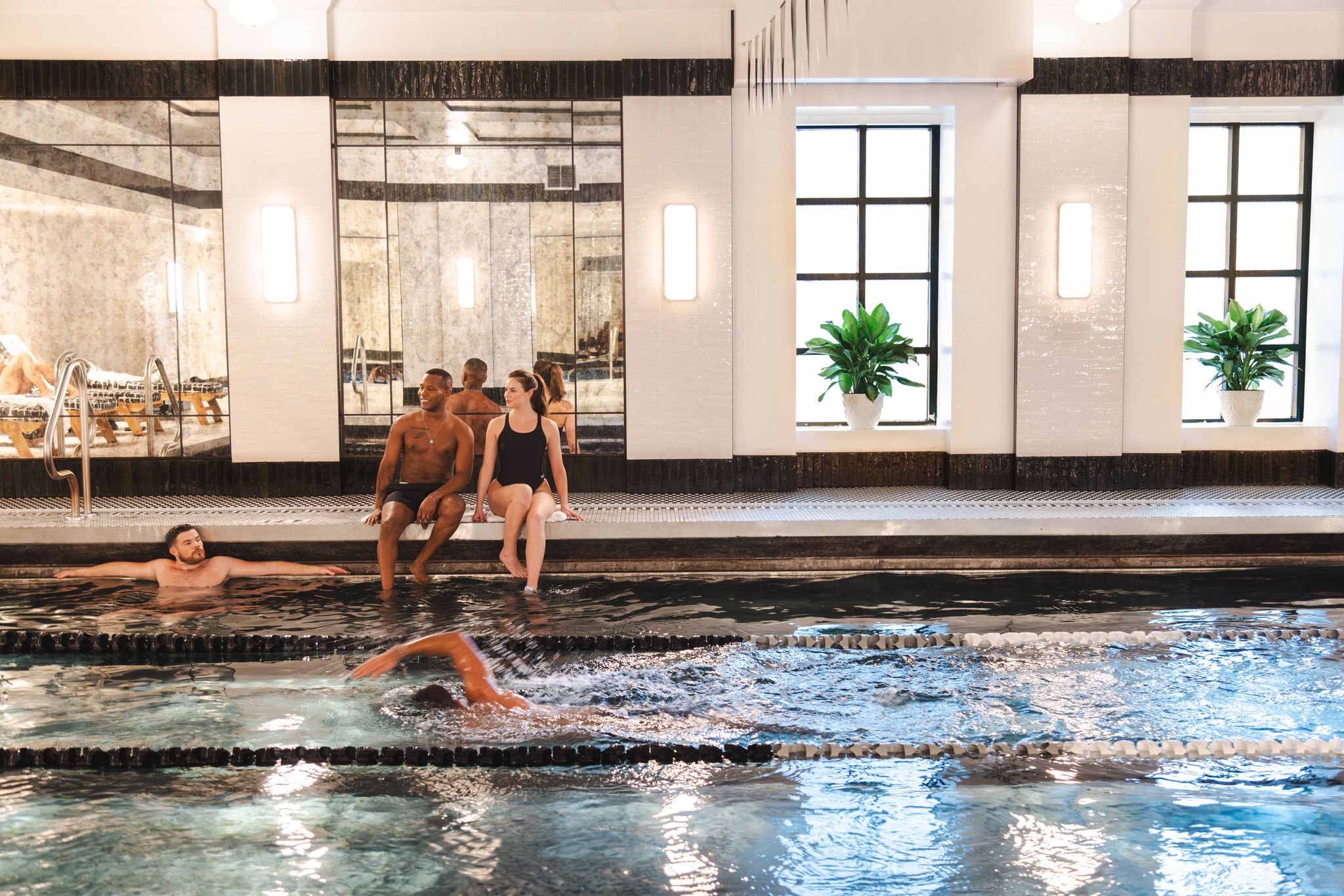 Two people watch a person swimming along a beautiful lap pool