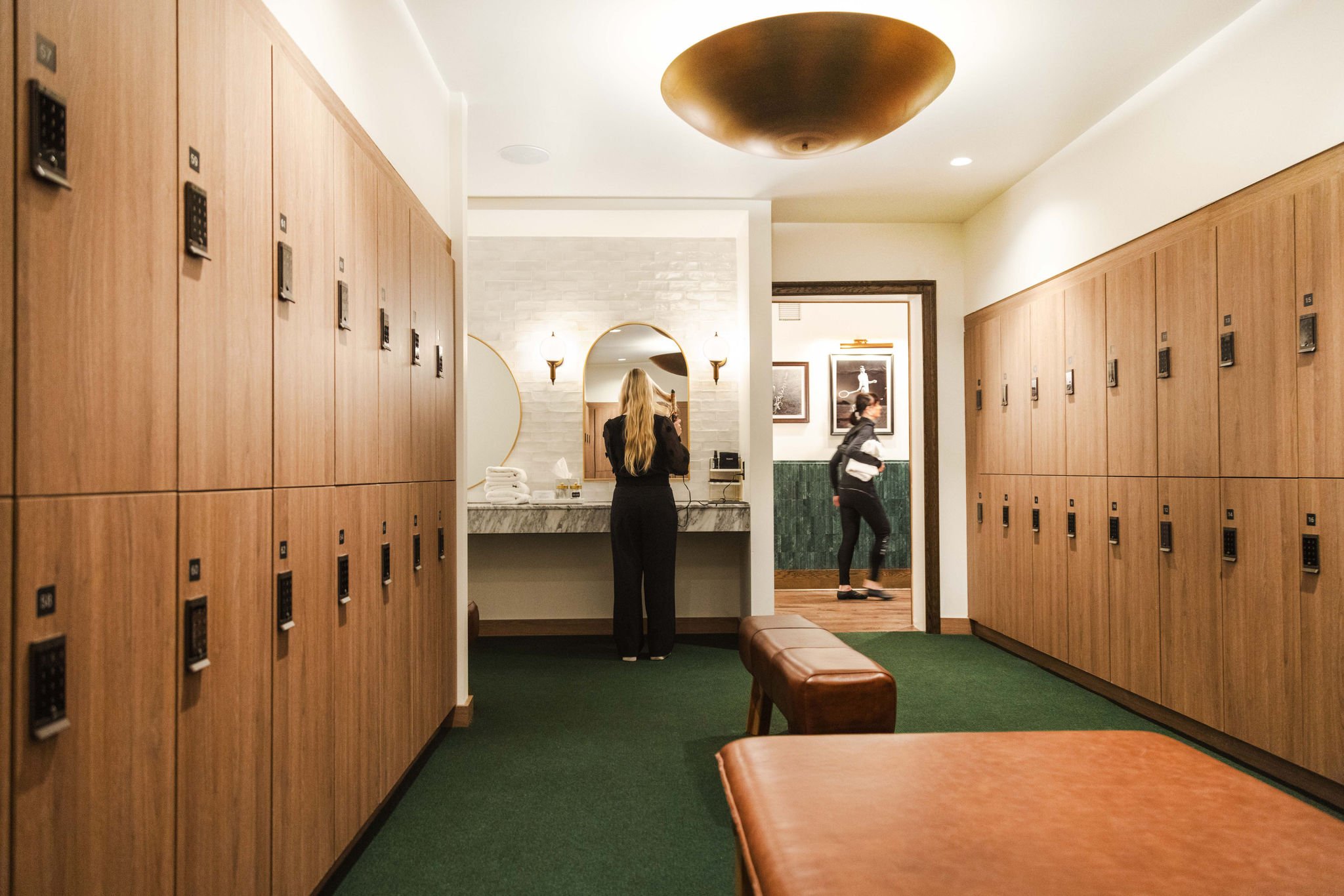 A woman fixing her hair facing away from the camera in a large, luxurious locker room