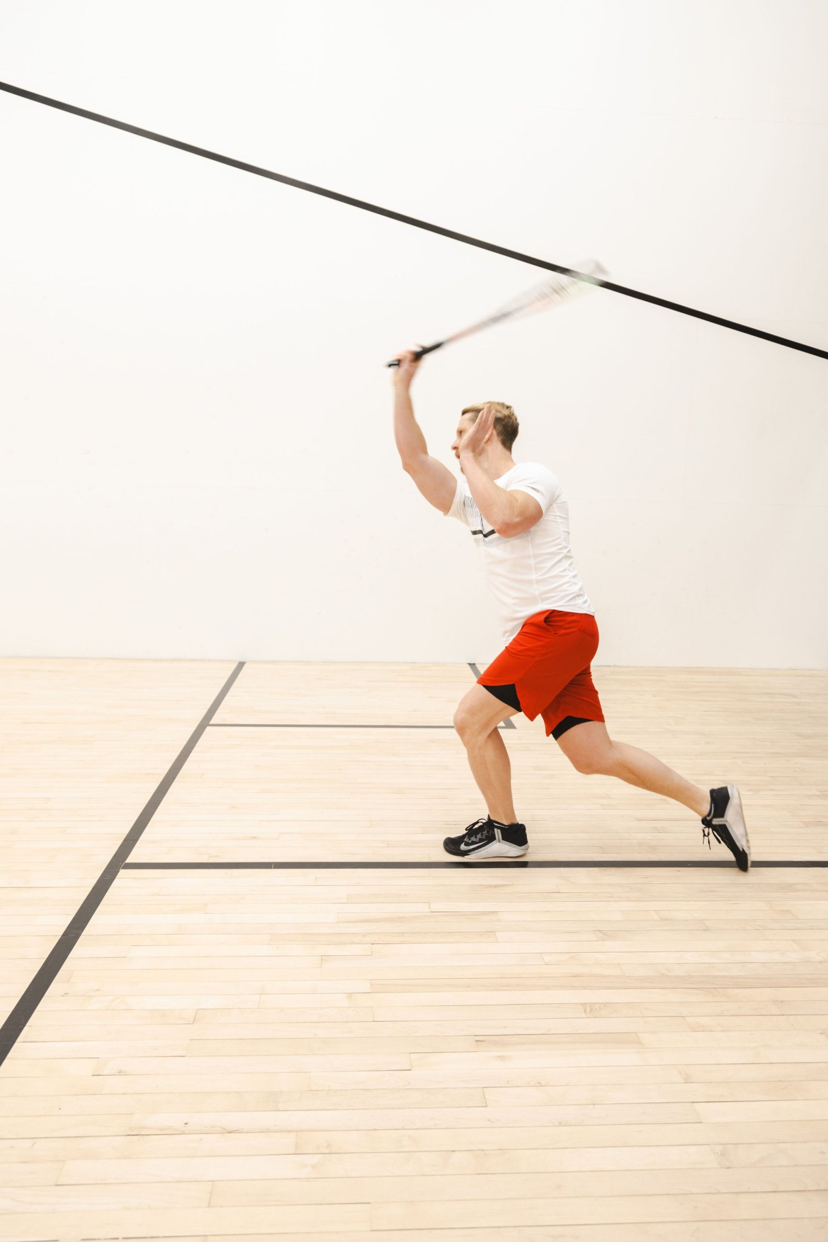 A man hitting a ball in a squash court. He is moving quickly and is blurred in action.