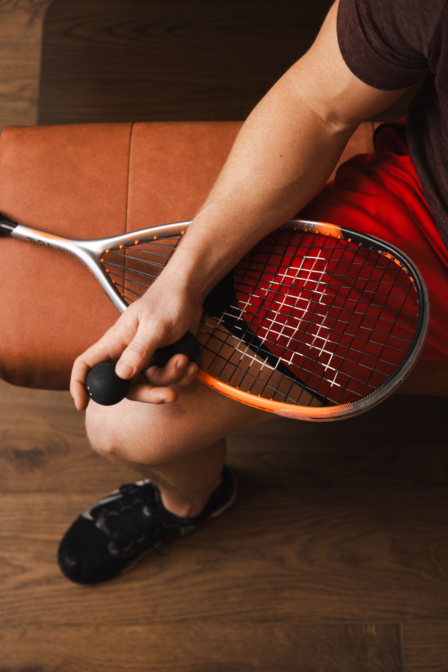 A shot of a man overhead holding a squash racquet and ball on a leather bench