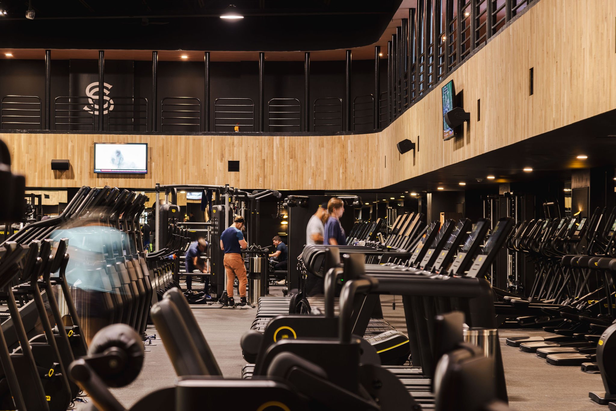 A double-height fitness floor packed with workout equipment and people working out