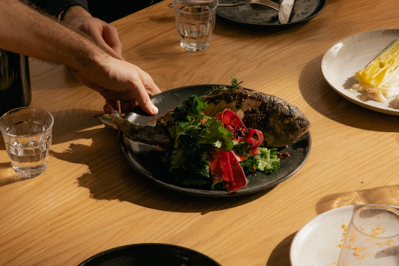 A server placing a fish dish on a table of other dishes