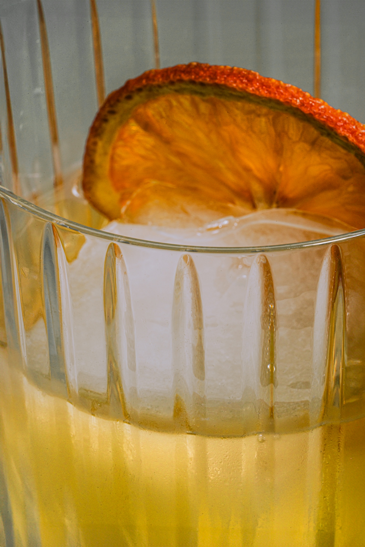 A closeup of a cocktail with a thin orange wheel and large cube of ice