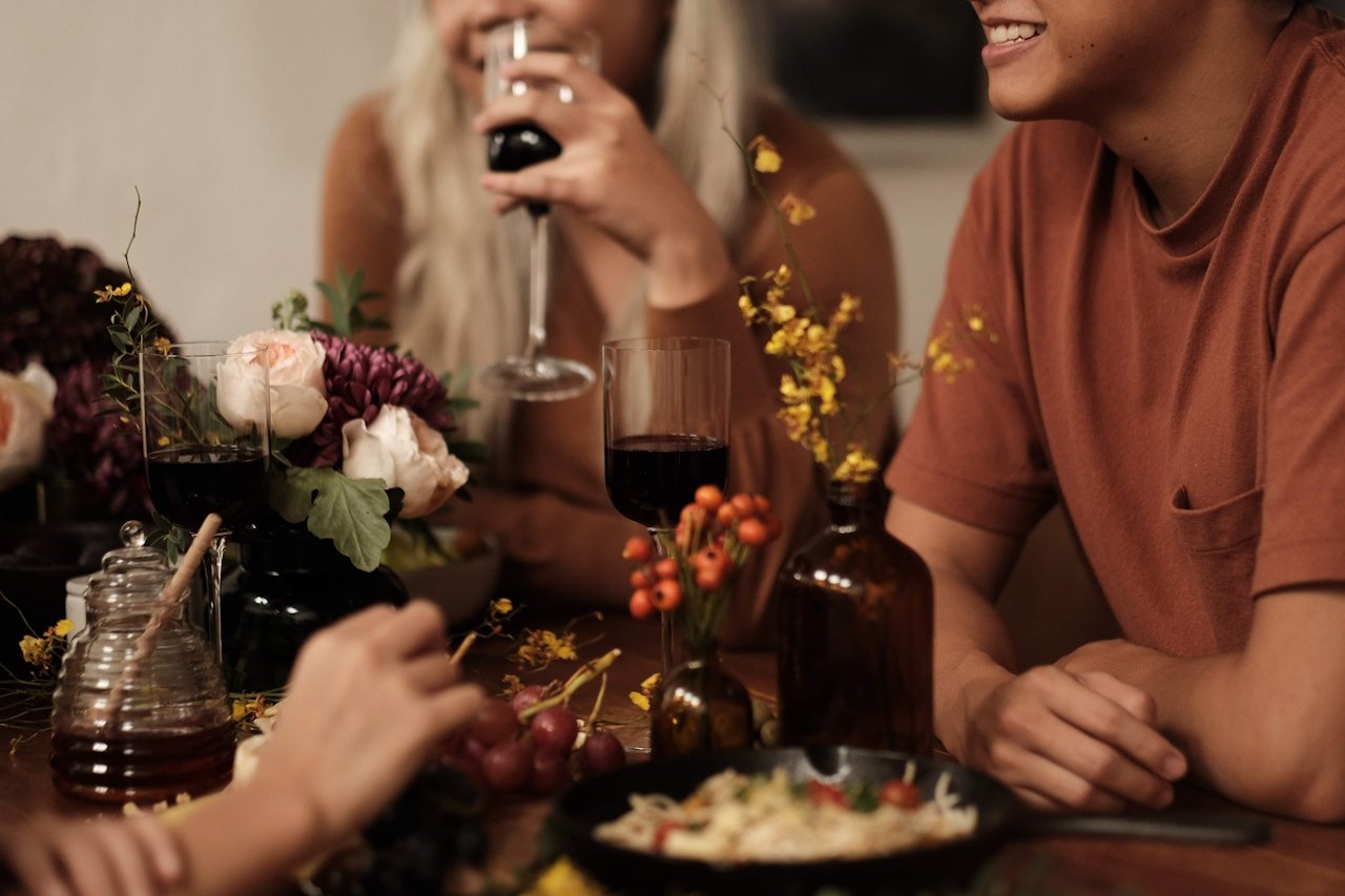 A small group of friends are enjoying a meal with flowers and glasses of red wine.