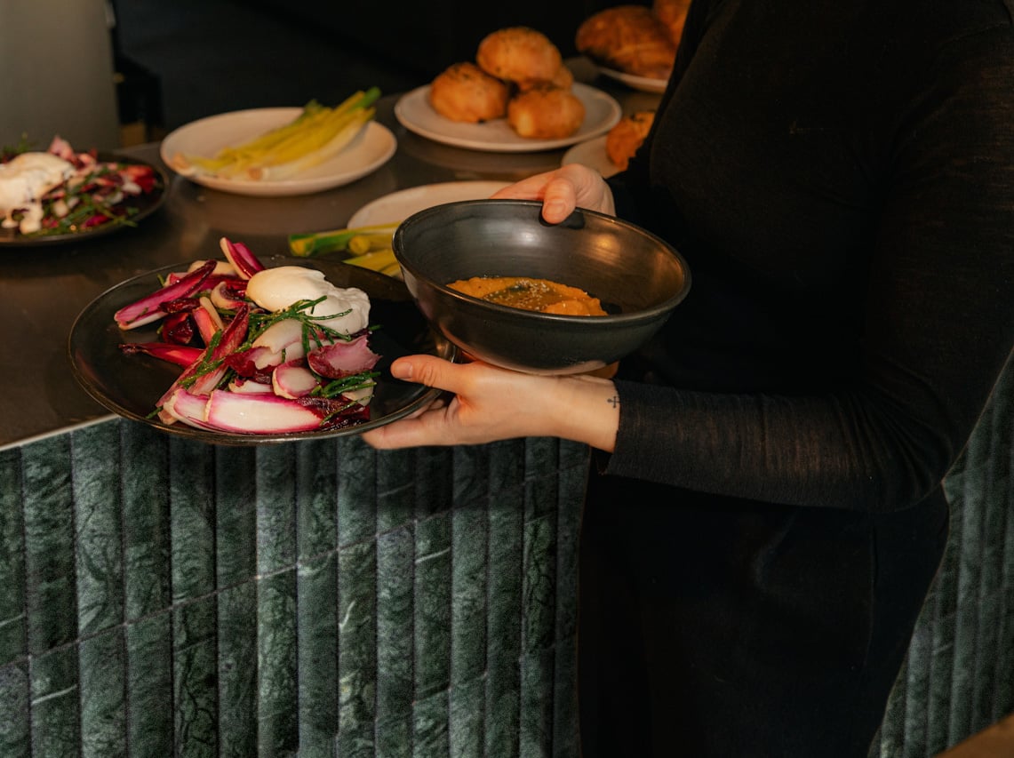 A server gathering dishes in front of a green marble bar