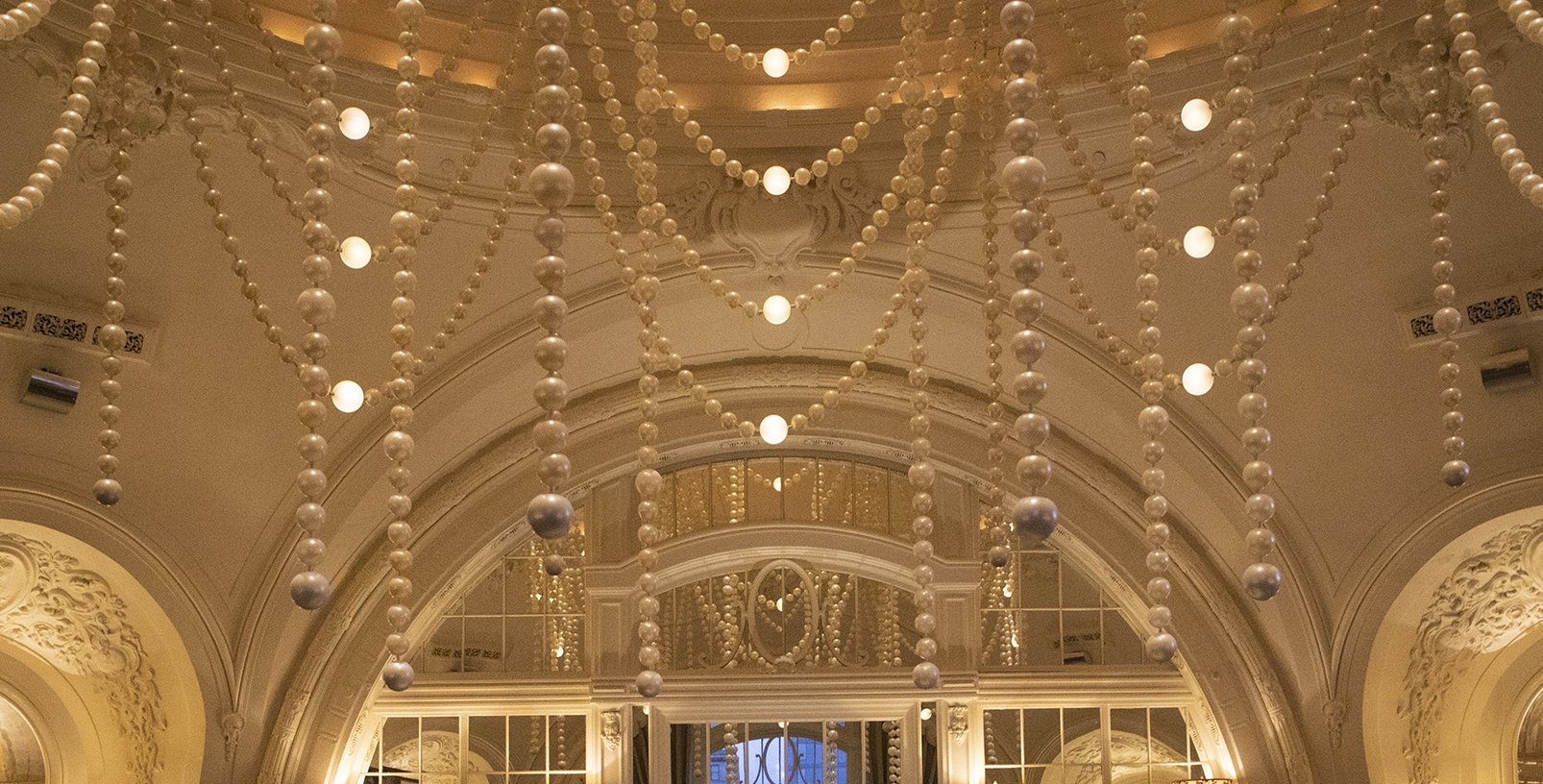 A circular room with a circular bar at the center. there are oversized pearls draped and hanging from the ceiling, and lit coves next to a large arched window